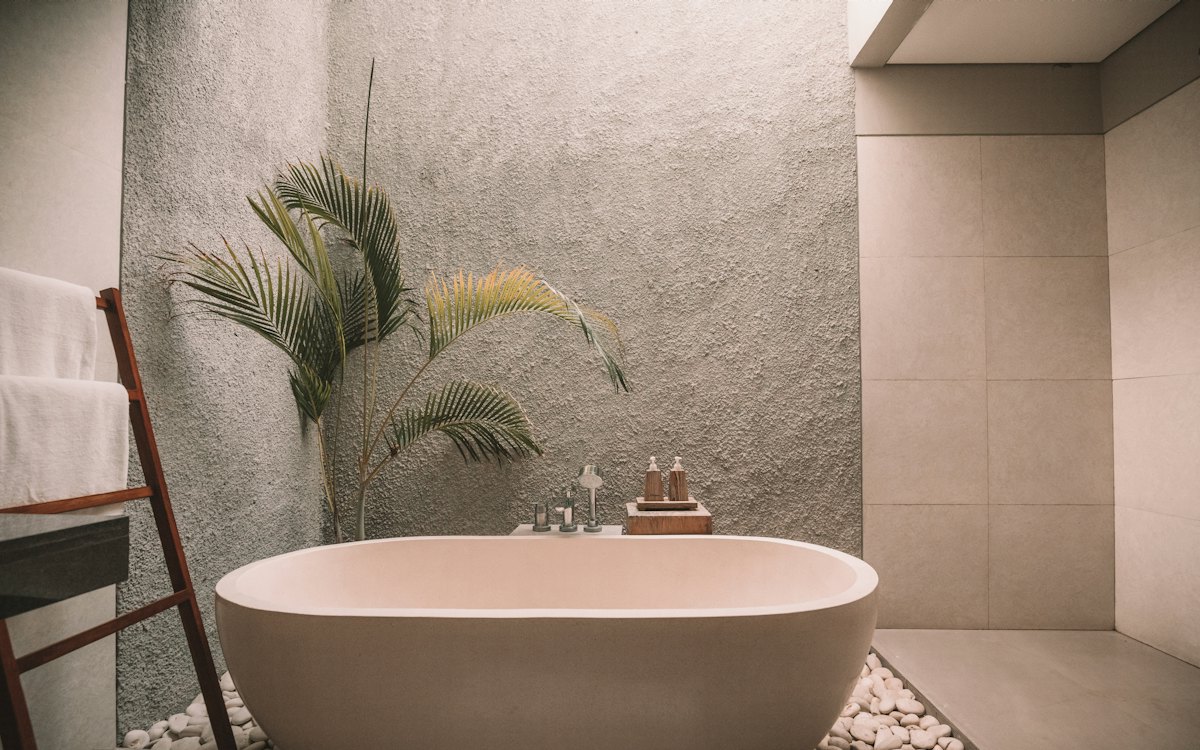 Photo: the family bathroom, with a freestanding bath, textured stone walls and a palm in the corner.
